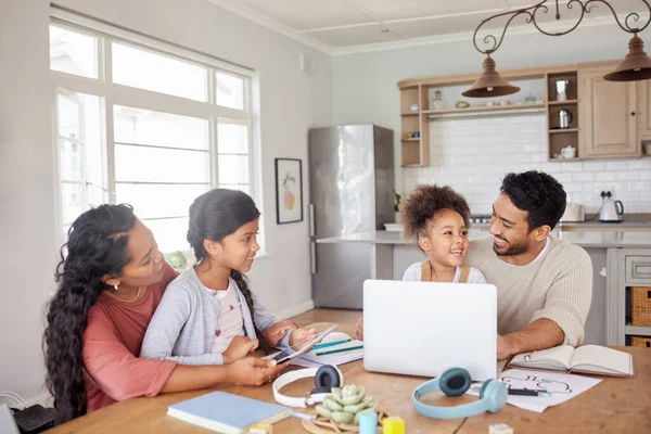 Mixed race family using information technology at home. Two little girls doing homework in the kitchen with help from their mother and father. Parents and children working on school work together.