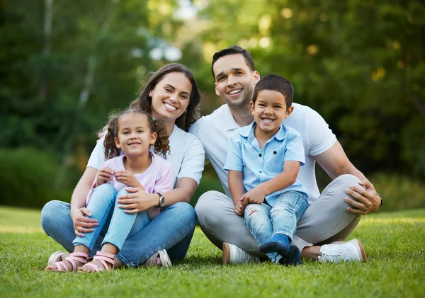 stock image Young happy mixed race family relaxing and sitting on grass in a park together. Loving parents spending time with their little children in a garden. Carefree siblings bonding with their mom and dad.