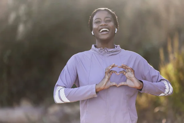 Black woman portrait, fitness and heart hand sign of a athlete showing love for nature and sports. Happy, excited and laughing sport woman on a run outdoor feeling freedom and gratitude from running.