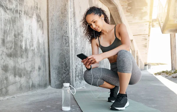 Hows my health stats looking. Full length shot of an attractive young woman crouching down and using her cellphone during her outdoor workout