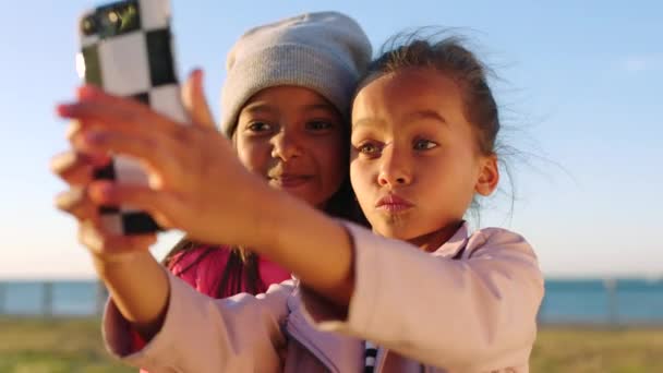 朋友和电话在海滨公园边亲自出马边张嘴做傻脸 用5G智能手机拍照的孩子 手机和女孩的个人资料 快乐的回忆或社交媒体 — 图库视频影像