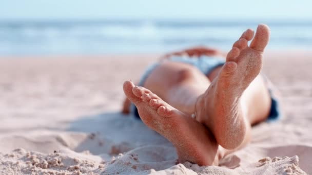 ビーチで夏休み 屋外での旅行や休暇旅行のためにリラックスしてください 裸の足 つま先とリラックスして太陽の日焼け 週末の休憩やモックアップでの休暇のために砂浜の海岸に横たわって — ストック動画