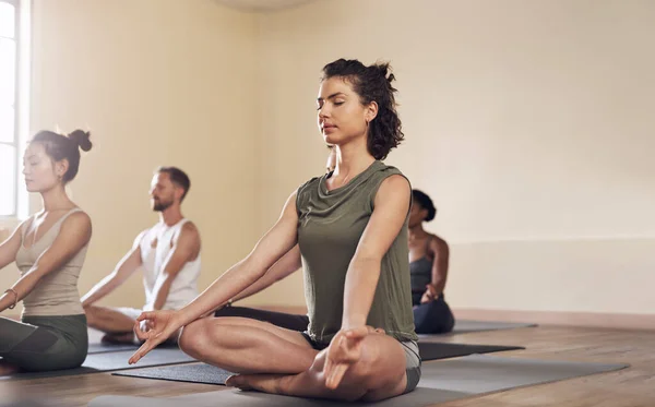 Life is less complicated when you meditate. Full length shot of a group of young people meditating and practicing yoga together inside a yoga studio