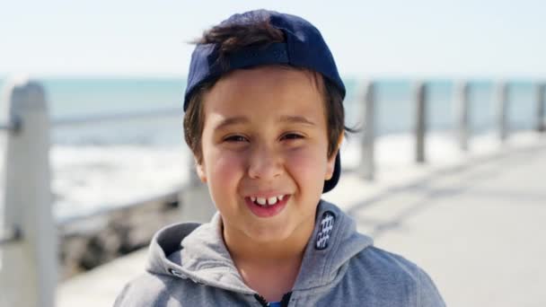 ビーチでの顔 幸せな子供休暇 または風の強い天候での旅行 カナダから来た少年のリラックスした自由と肖像画で 屋外の遊歩道にキャップが立っています — ストック動画