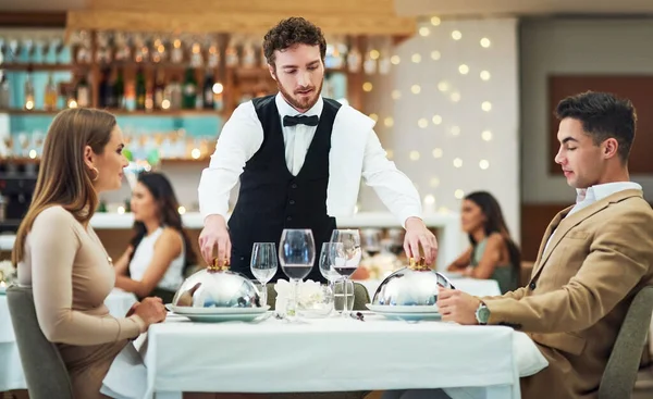 Allow me to serve you. a handsome young waiter serving a young couple in a restaurant