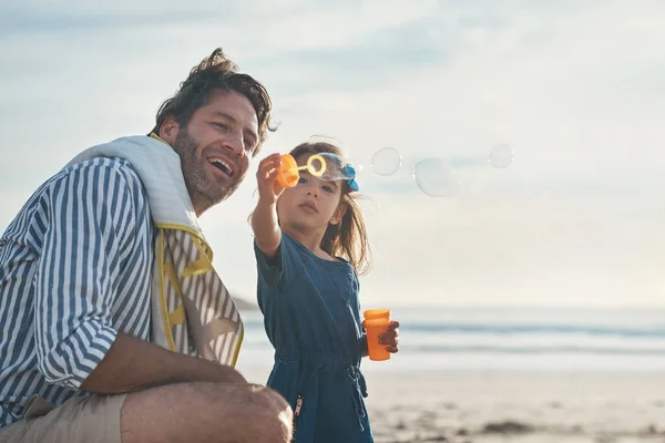 Dad, look what I can do. a playful mature father blowing bubbles with his daughter during a day out on the beach together