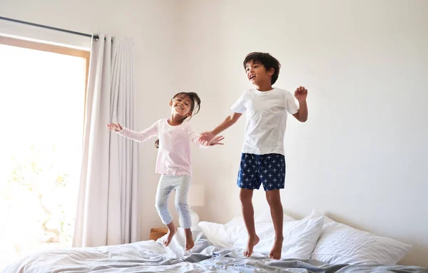 No parents, no rules. Full length shot of a young brother and sister jumping on bed together at home