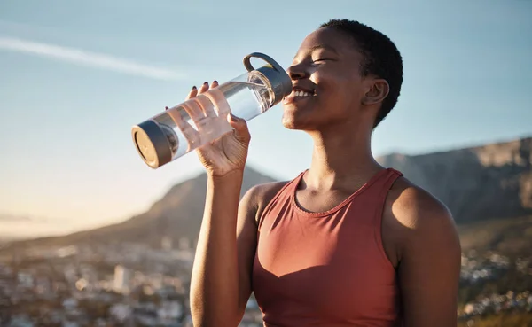 Black woman, runner and drinking water for outdoor exercise, training workout or marathon running recovery. African woman, healthy athlete and hydrate with bottle for fitness, health and cardio run.