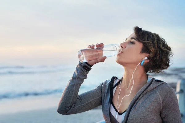 Take a sip and go again. a young woman drinking water after her run