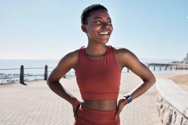 black woman, happy and thinking on beach sidewalk for fitness motivation, mental health and runner rest outdoor. African woman, athlete smiling and confident mindset vision by Cape Town seaside.