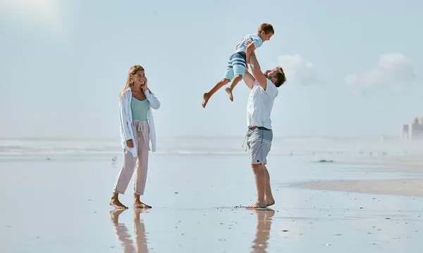 Family, beach and father lifting kid on vacation, holiday or summer trip outdoors. Love, support and care of mother, man and boy playing, bonding and having fun while enjoying quality time together.