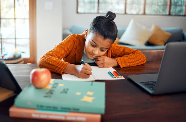 Education, home school and distance learning with a student girl writing in her book during an online class. Laptop, study and kids with a female pupil or child learner in her house for development.