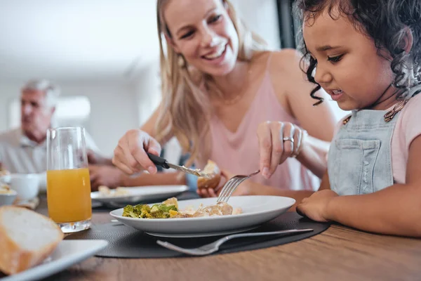 Family, mother and cutting food for girl while having lunch at dinner table in home. Love, foster care and happy mom helping child with eating, smiling and enjoying a delicious meal together in house.