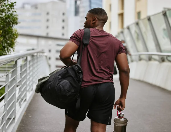 Black man, back or fitness bag on city bridge, road or street with workout gear, training water bottle or exercise kit. Runner, sports athlete or personal trainer in urban travel to gym for wellness.