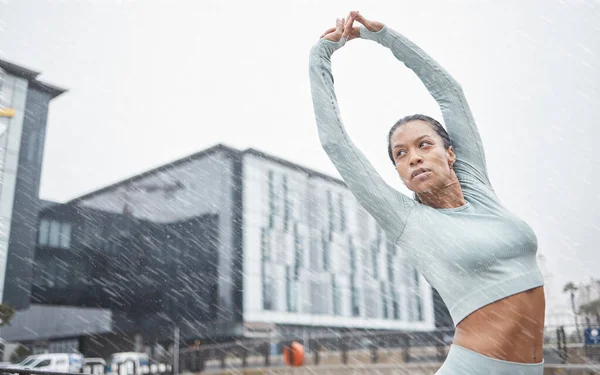Black woman, stretching and fitness in rain and city for running training for a marathon. Workout, exercise and run goal motivation of a woman athlete and runner doing sports in winter health warm up.