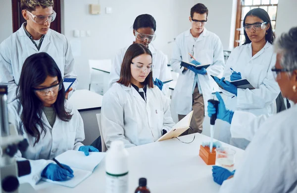 Science, students and education in a medical laboratory writing notes during scientist lecture or lesson with mentor or teacher. Medical men and women for training and learning in chemistry class.