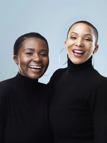 Polo necks suit us we know. Portrait of two beautiful young women holding each other while standing against a grey background