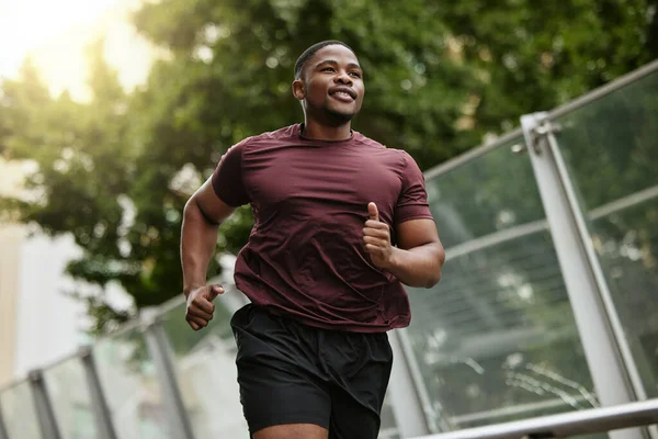 Black man, fitness and running in park for healthy workout, exercise or cardio in the nature outdoors. Happy African American male runner enjoying a jog, run or exercising for health and wellness.