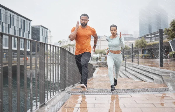 Fitness, city and couple in the rain running for workout, marathon training and exercise in winter. Sports, wellness and man and woman run for endurance, challenge and body performance in urban town.