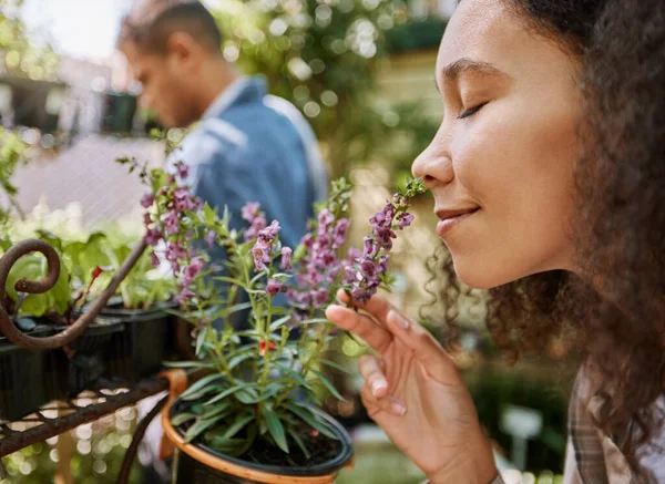 Smelling, plants and face of a woman at a nursery, flower shopping and aroma at a garden market. Happy, peace and girl with smell of flowers, pot plant and floral heather ecology at a gardening shop.