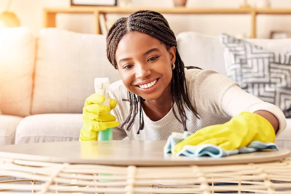 Smile, spray bottle and black woman cleaning table with gloves and alcohol solution in living room. Coffee table, spring cleaning and happy woman wiping dust in home for safety from bacteria and germ.