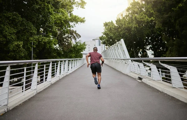 Fitness, man and running in the city park for healthy exercise, cardio workout or training in the outdoors. Active athletic male runner in sports activity, run or exercising outside on city bridge.