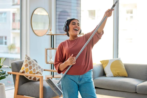 Dance, radio or woman cleaning with music for singing or listening to a song with broom as a guitar at home. Relax, freedom or happy Indian girl cleaner streaming audio on headphones or housekeeping.