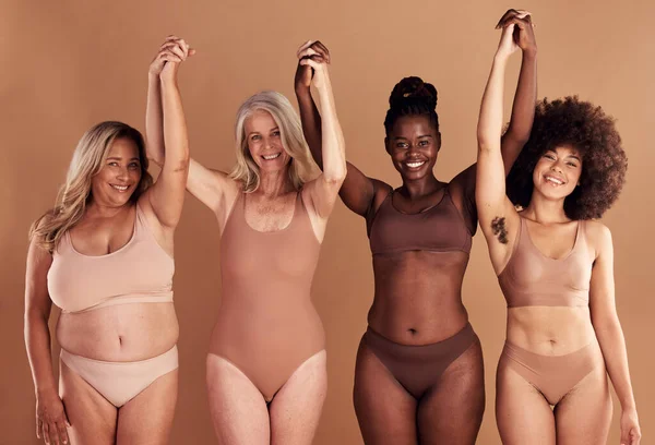 Beauty, diversity and natural with woman friends in studio on a beige background with their hands raised in celebration. Wellness, underwear and real with a model female group standing together.