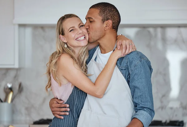 Love, interracial and couple kiss in kitchen, happiness and loving together for relationship. Romance, man and woman with embrace, kissing and celebrate for anniversary, cooking and relax with hug