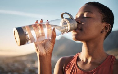 Spor, siyah kadın ve idmandan sonra su şişesi içmek, egzersiz ve açık hava kardiyo çalışması. Susamış genç sporcu, spor susuzluğu ve sağlıklı yaşam için beslenme, sağlıklı vücut ve enerji.