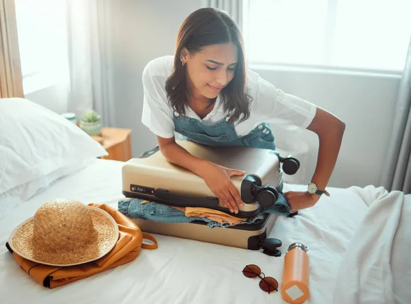 Woman, overloaded suitcase and luggage bag in bedroom for travel, vacation and international journey, holiday and trip. Female tourist struggle to close baggage full of clothing, packing and problem.