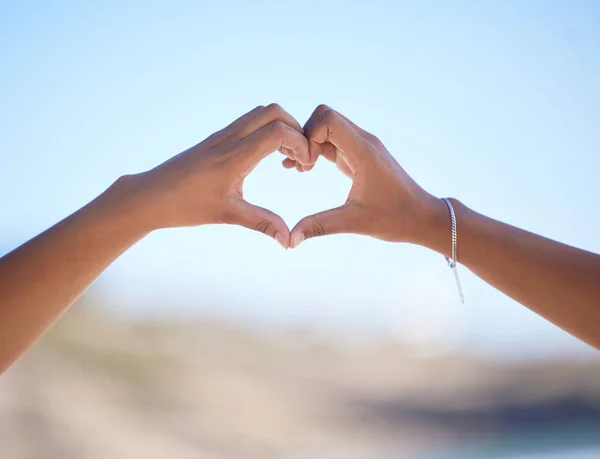 Hands together, heart sign and outdoor at beach, nature and blue sky in blurred background for love. Couple, hand touch and romantic gesture for bonding, care and support for relationship in Miami.