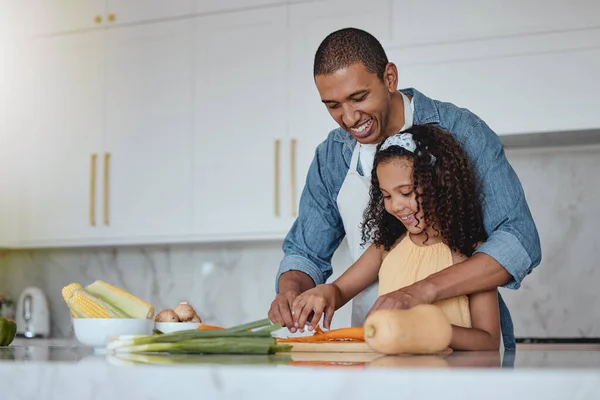 Love, father and girl cooking food with healthy vegetables for lunch or dinner meal as a happy family at home. Nutrition, smile or dad teaching or helping a young child cut carrots on kitchen counter.