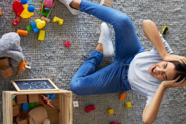 Tired, stress and frustrated mom with fatigue and headache cleaning children toys. Above view of mama and woman scream from kids mess in a home living room feeling overwhelmed burnout from motherhood.