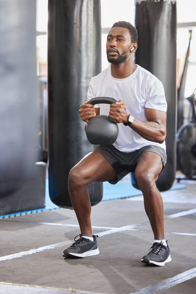Black man, gym and kettlebell for squat exercise, weightlifting workout or muscle growth training. African bodybuilder, wellness trainer and metal weights for strong legs, body development or health.