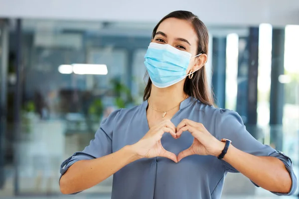 Covid, employee or woman with heart sign or hand gesture in office building showing support, love or safety. Compliance, coronavirus or happy worker in face mask with peace, wellness or care at job.