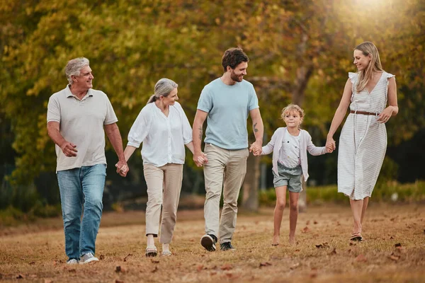 Family, walking and holding hands outdoor with mother, dad and girl happy with grandparents. Happy family, love and parent care in nature with a child in a grass field park in autumn on holiday.
