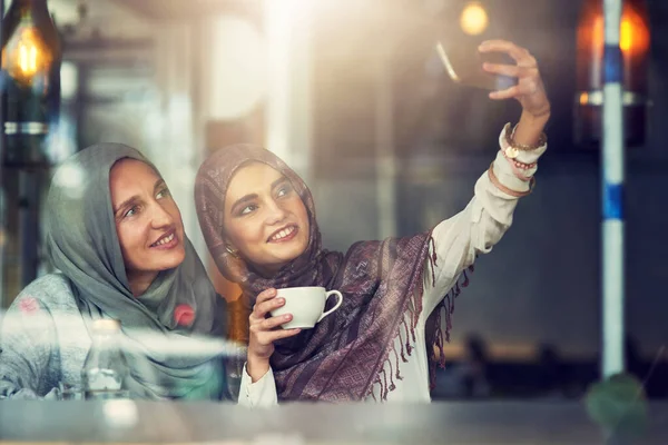 We go together like coffee and cream. two women taking selfies with a mobile phone in a cafe