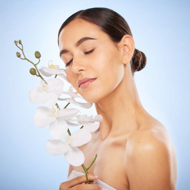 Beauty, skincare and woman with an orchid in a studio for a health, wellness and natural face routine. Cosmetic, self care and girl model with clear skin from spa facial treatment by blue background clipart