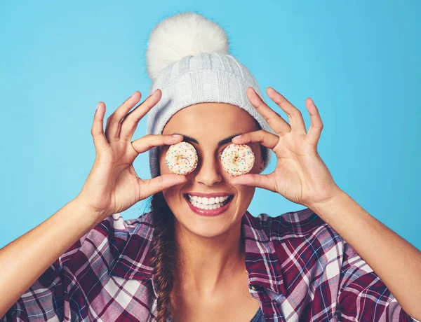You sure are sweet on the eyes. a young woman covering her eyes with cookies against a colorful background