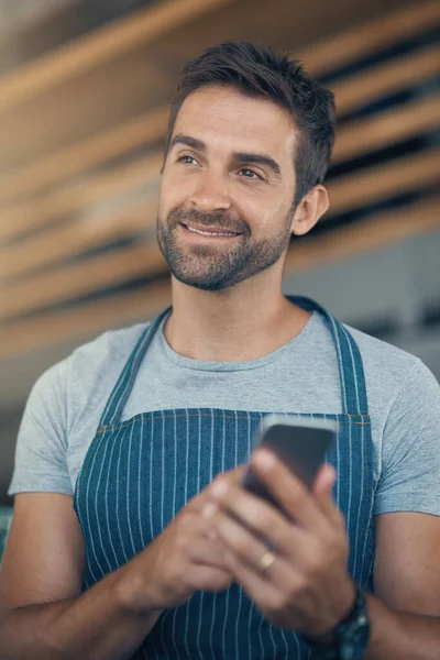 Running a coffee shop with smart apps. a young man using a mobile phone while working at a coffee shop
