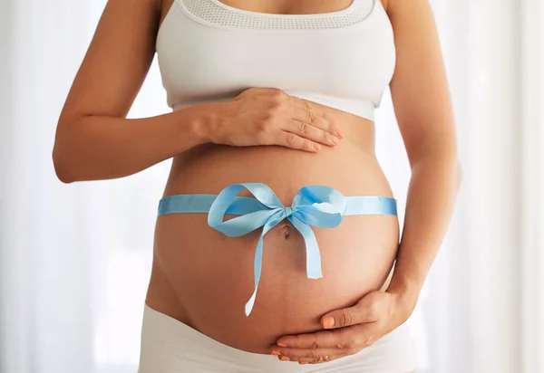 Theres no bigger gift. a woman with a blue ribbon tied around her pregnant belly