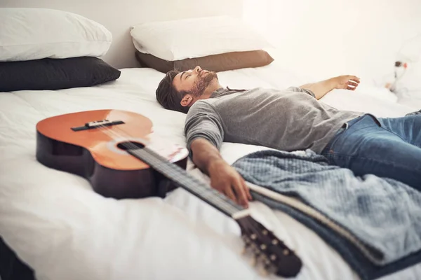 Quick nap before I start playing again. a young handsome man sleeping next to his guitar at home