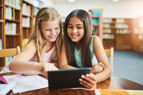 This really helps with homework. two cheerful young school girls working together in a classroom with a digital tablet at school during the day