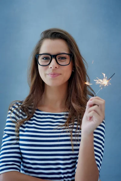 Dont be afraid to sparkle. Studio shot of a beautiful young woman holding sparklers against a blue background