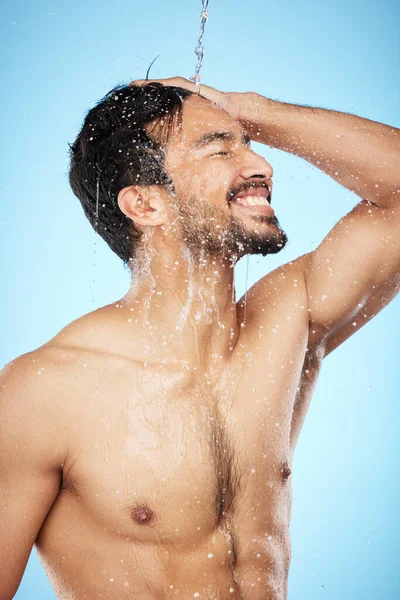 Face, water splash and man in shower cleaning for body care in studio isolated on a blue background. Hygiene, skincare and profile of male model bathing and washing for health, wellness and beauty