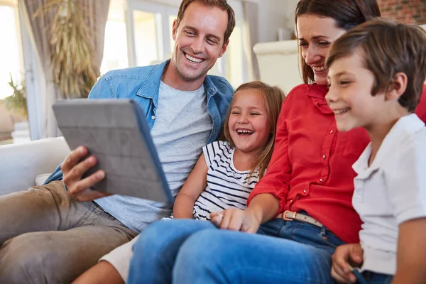 Family entertainment at a touch. smiling parents sitting with their young son and daughter on their living room sofa at home using a digital tablet