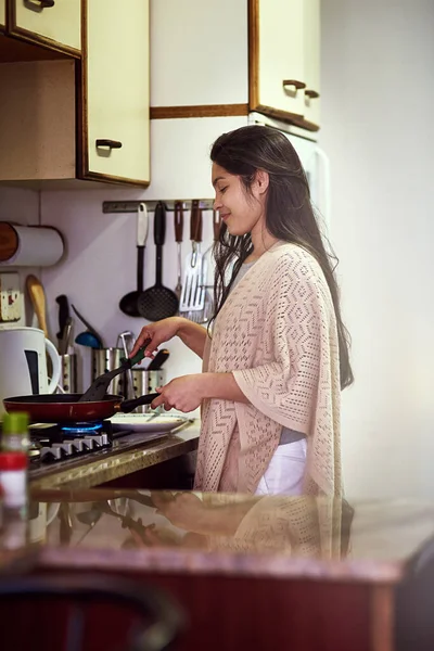 Cooking up something scrumptious for breakfast. a happy young woman cooking breakfast in her kitchen at home