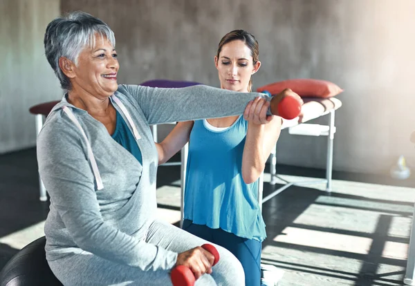 Preventing age related muscle weakness with regular physiotherapy. a senior woman using weights and a fitness ball with the help of a physical therapist