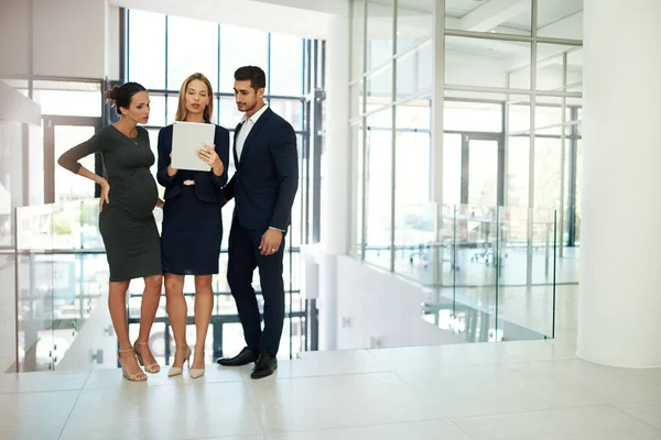 Great things get done when people come together. Full length shot of a group of young businesspeople standing together in a modern office and using a tablet